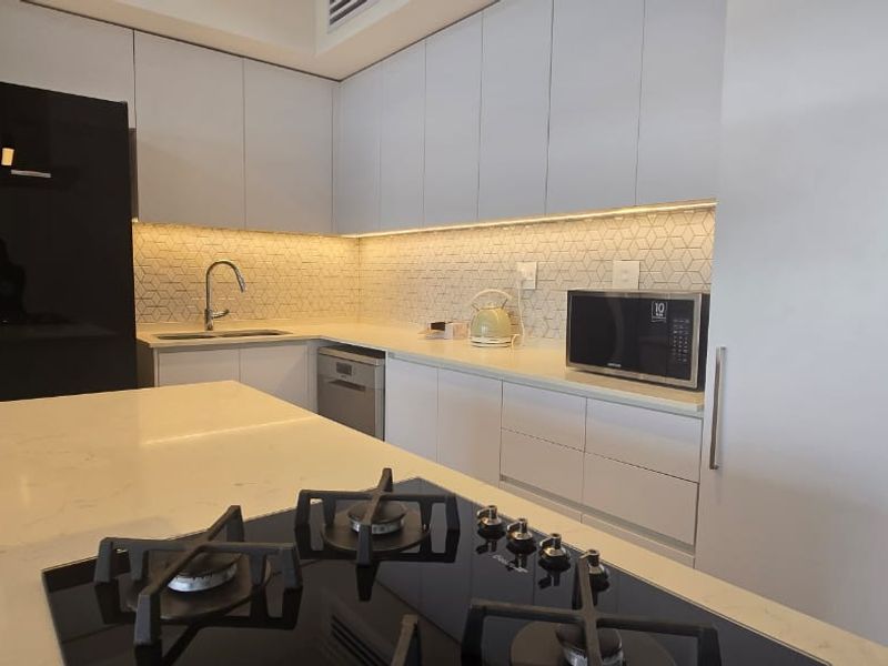 Modern kitchen featuring sleek white cabinetry, stone countertops, a central island with a gas hob, and a stylish geometric tiled backsplash.