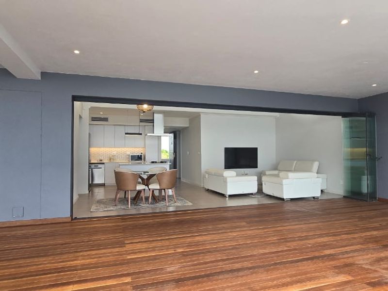 Spacious open-plan living area featuring timber decking, seamless indoor-outdoor flow through stacking glass doors, and a modern kitchen with integrated cabinetry.