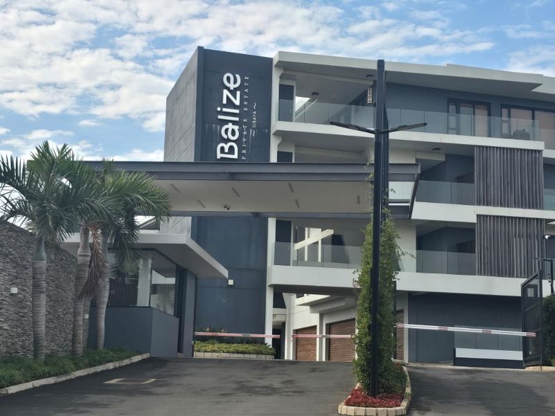 Modern apartment complex entrance featuring contemporary architectural design, stone cladding, glass balustrades, and a secure gated driveway access.