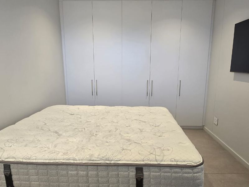 A clean bedroom featuring neutral walls, tiled flooring, and ample built-in cupboard storage space.