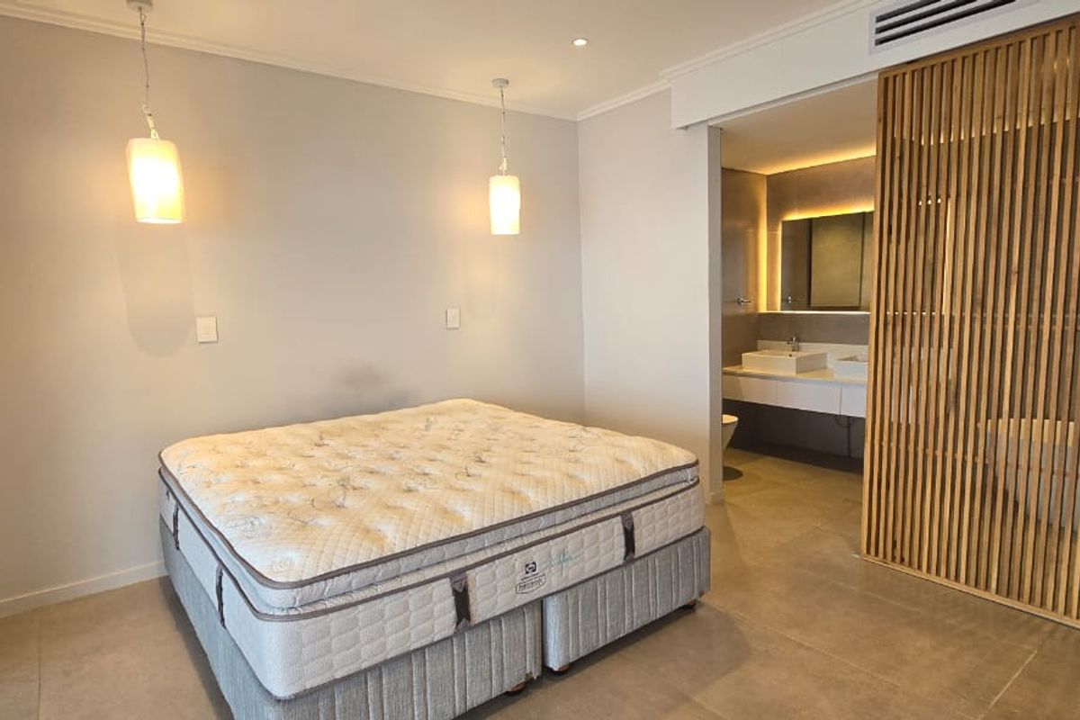 Modern bedroom featuring tiled flooring, pendant lighting, and a stylish timber slat divider separating the space from an open-plan en-suite bathroom.