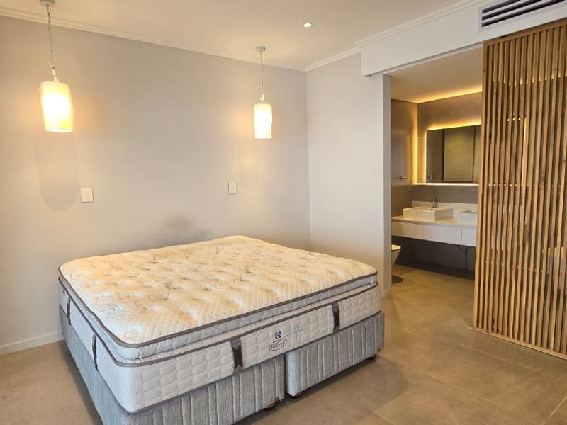 Modern bedroom featuring tiled flooring, pendant lighting, and a stylish timber slat divider separating the space from an open-plan en-suite bathroom.