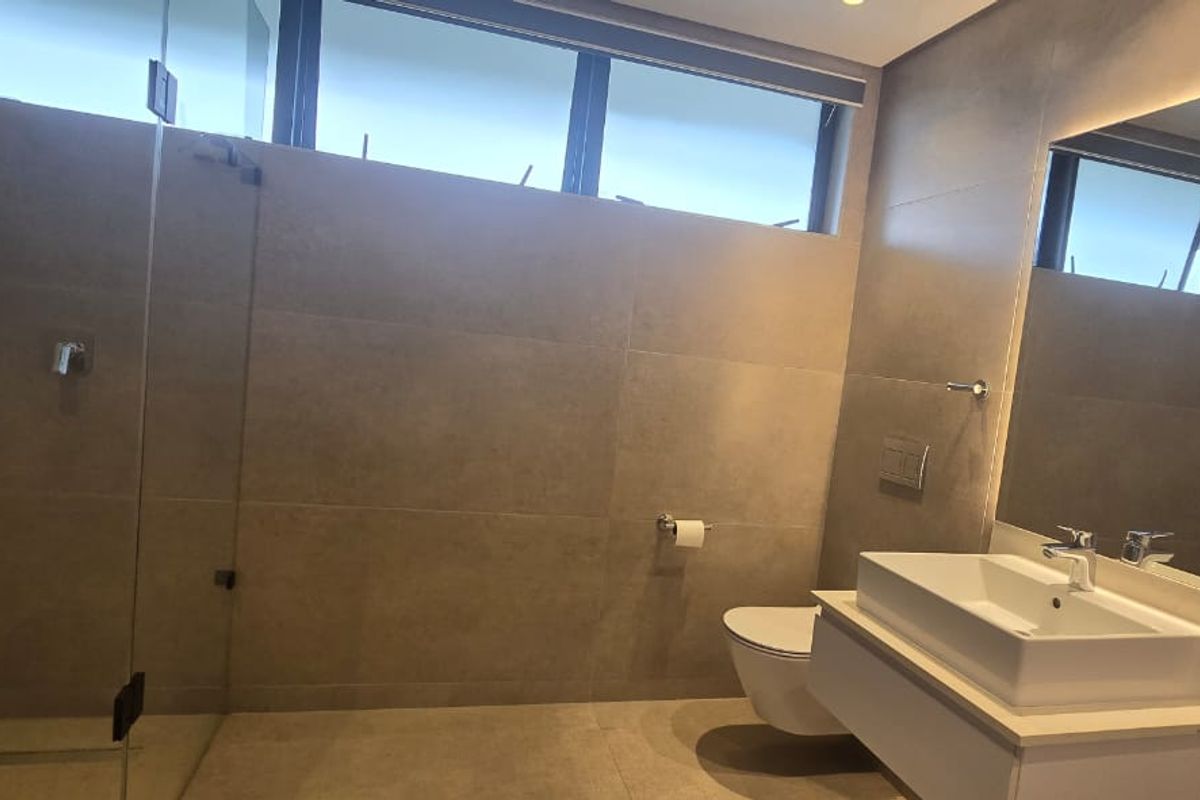 Modern bathroom featuring a floating vanity with vessel sink, wall-hung toilet with concealed cistern, glass shower enclosure, and large format neutral tiling.