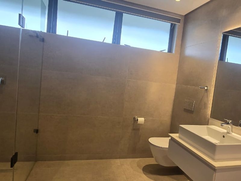 Modern bathroom featuring a floating vanity with vessel sink, wall-hung toilet with concealed cistern, glass shower enclosure, and large format neutral tiling.