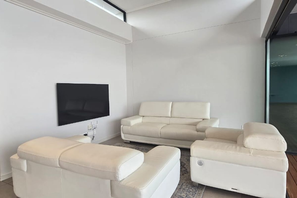 A bright living room featuring tiled flooring, a high clerestory window for natural light, and a sliding glass door leading to an outdoor area.