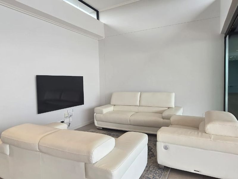 A bright living room featuring tiled flooring, a high clerestory window for natural light, and a sliding glass door leading to an outdoor area.
