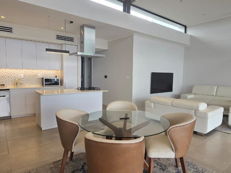 Modern open-plan living area featuring a sleek kitchen with island, gas hob, and integrated cabinetry, flowing into a bright, spacious lounge and dining area.