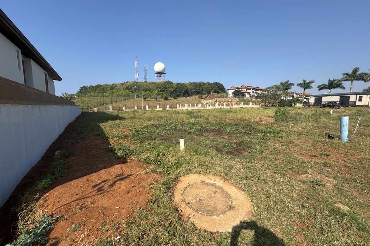A view of a vacant residential plot featuring a retaining wall, utility access points, and surrounding landscape.