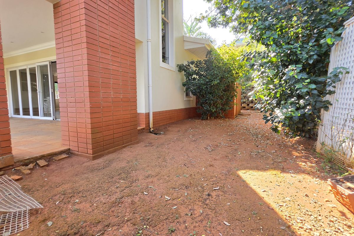 Rear exterior view of the townhouse featuring a covered patio area, brick facade, and an unlandscaped garden space requiring attention.
