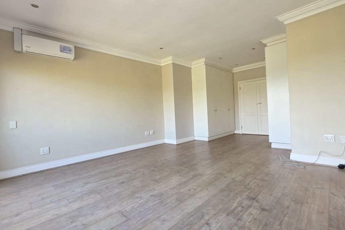 Spacious living area featuring laminate flooring, built-in storage cupboards, and an installed air conditioning unit, offering a clean and neutral blank canvas.