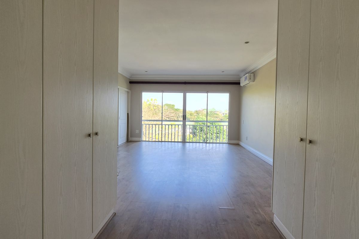 Spacious bedroom featuring built-in cupboards, laminate flooring, and a sliding glass door leading to a balcony with an air conditioning unit.