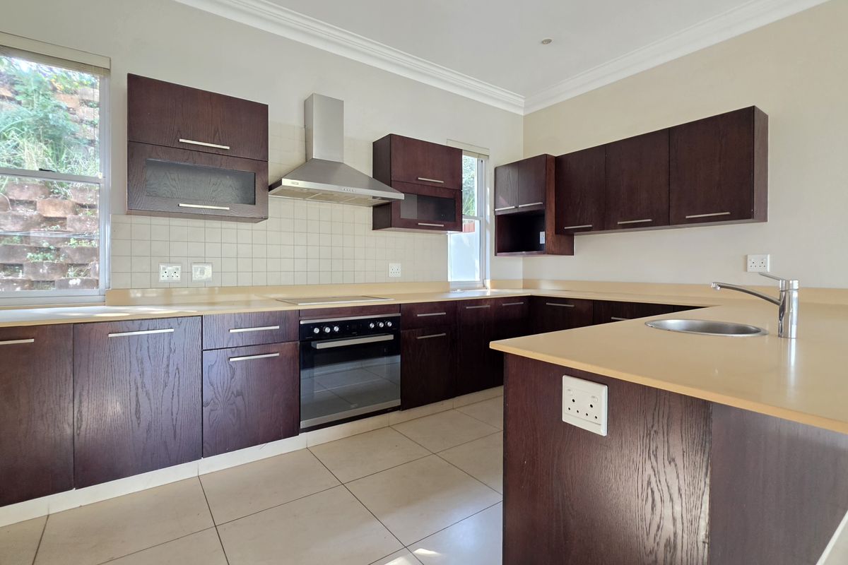 A clean, functional kitchen featuring dark wood cabinetry, built-in oven, extractor fan, and ample countertop space with a neutral tile backsplash.