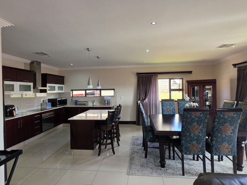 Spacious open-plan kitchen and dining area featuring dark cabinetry, a central island, tiled flooring, and direct access to the outdoor space.