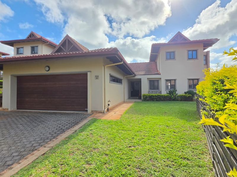 Front exterior view of a townhouse featuring a double garage, paved driveway, well-maintained lawn, and a tiled roof structure.