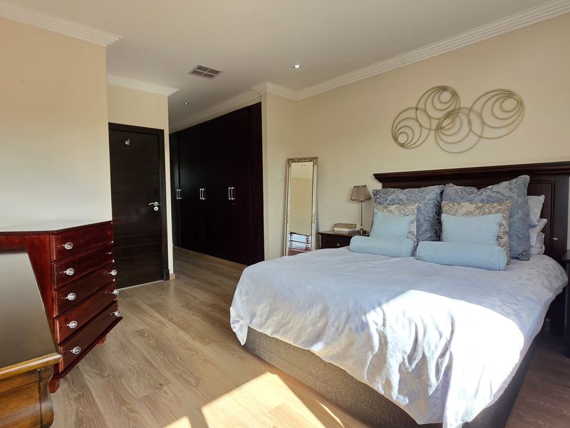 Spacious bedroom featuring light laminate flooring, extensive dark wood built-in cupboards, and elegant crown molding with recessed lighting.