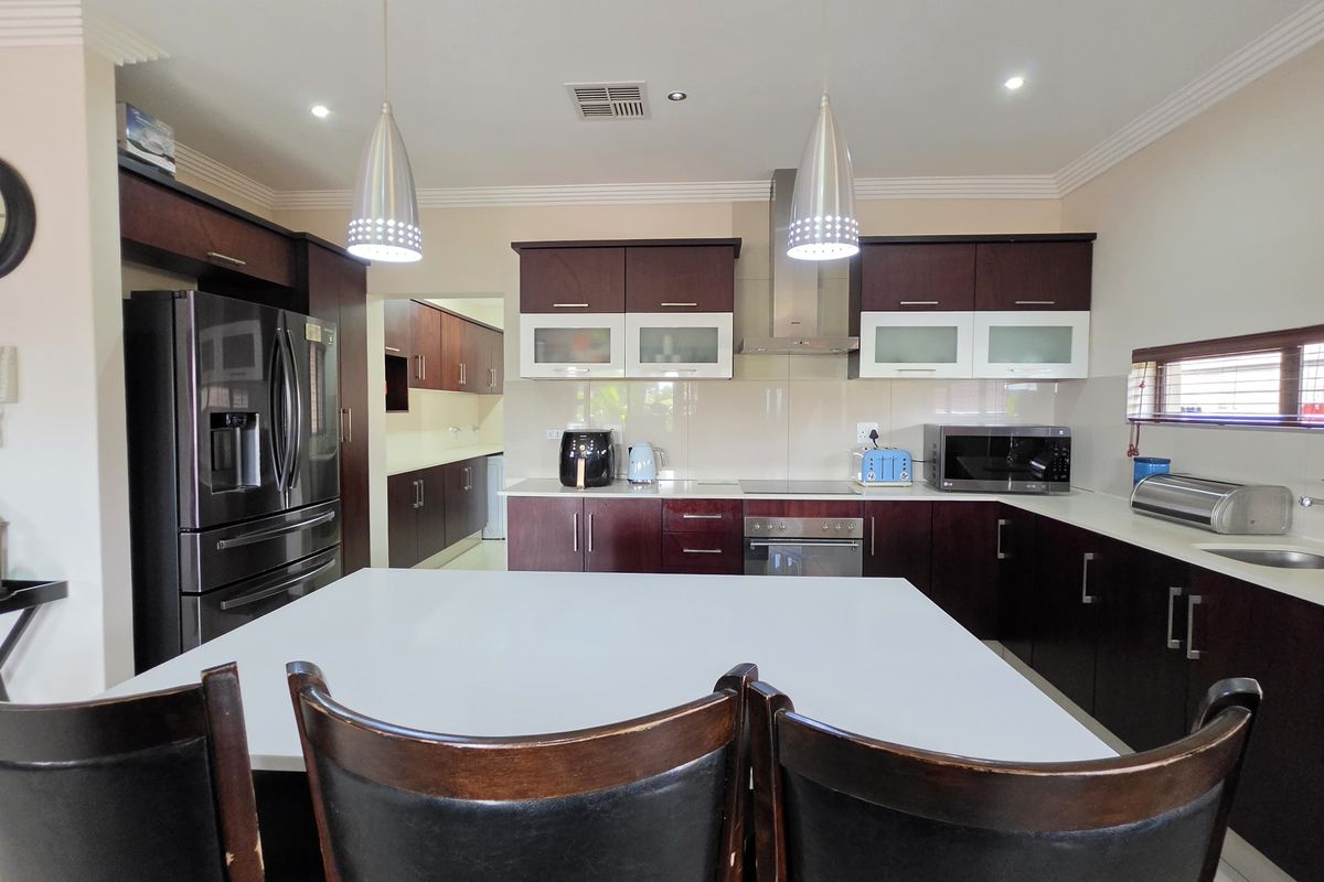 Modern kitchen featuring dark wood cabinetry, stone countertops, stainless steel appliances, and a central island, complemented by stylish pendant lighting.