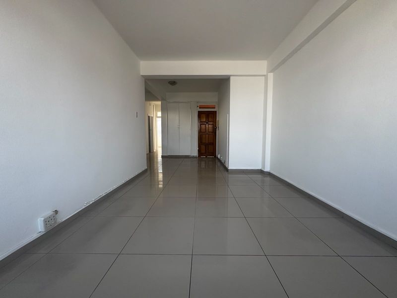 A bright, vacant living area featuring neutral tiled flooring, clean white walls, and a solid timber entrance door.