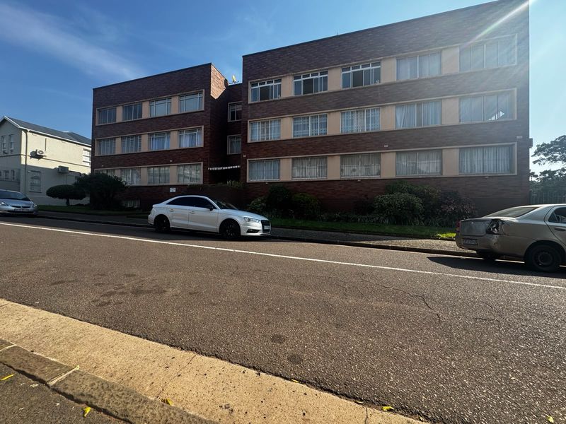 Street-level view of a multi-story brick apartment building featuring a classic facade with multiple window rows.