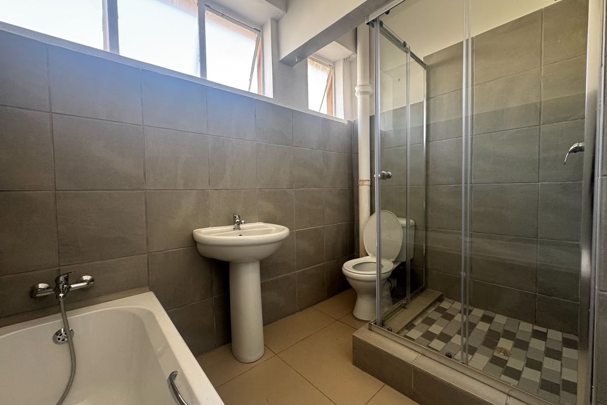 A functional bathroom featuring a pedestal basin, separate bathtub, and a glass-enclosed shower with tiled finishes throughout.