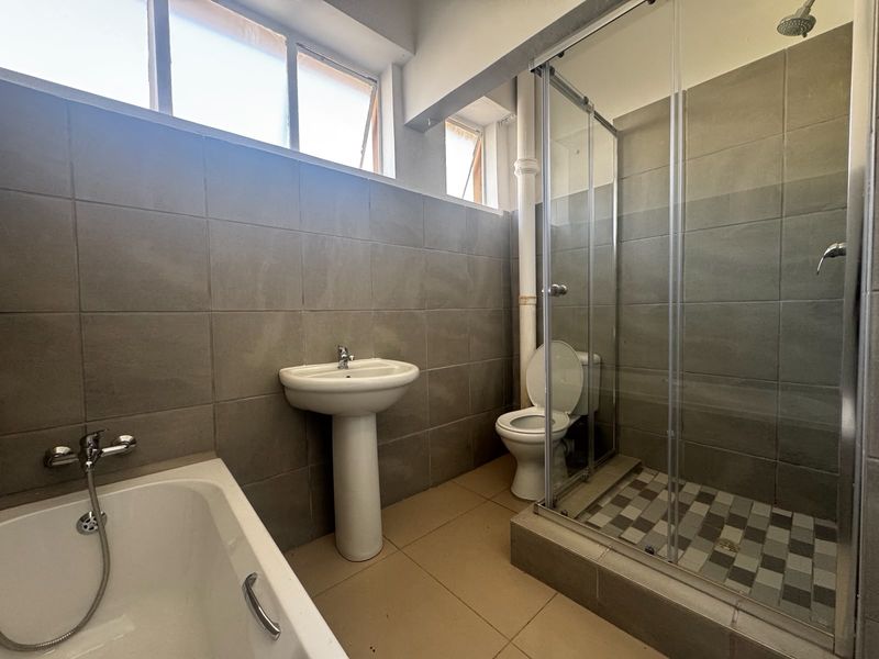 A functional bathroom featuring a pedestal basin, separate bathtub, and a glass-enclosed shower with tiled finishes throughout.