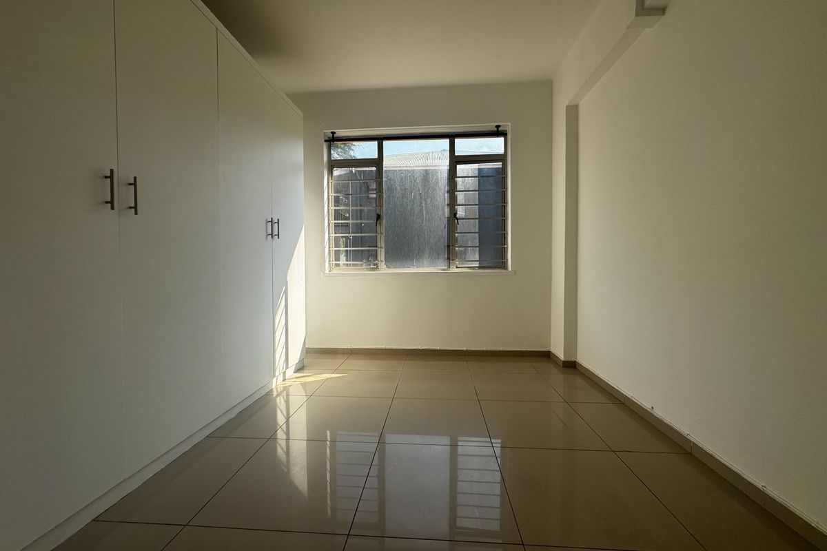 A bright, empty bedroom featuring neutral tiled flooring and extensive built-in cupboard storage, offering a clean and versatile space.