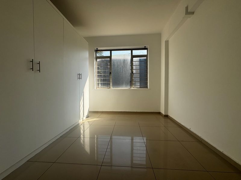 A bright, empty bedroom featuring neutral tiled flooring and extensive built-in cupboard storage, offering a clean and versatile space.