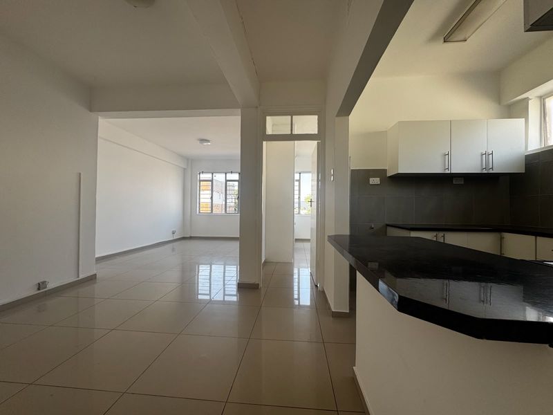 An open-plan living and kitchen area featuring tiled floors, modern cabinetry, and a breakfast bar, offering a bright and versatile living space.