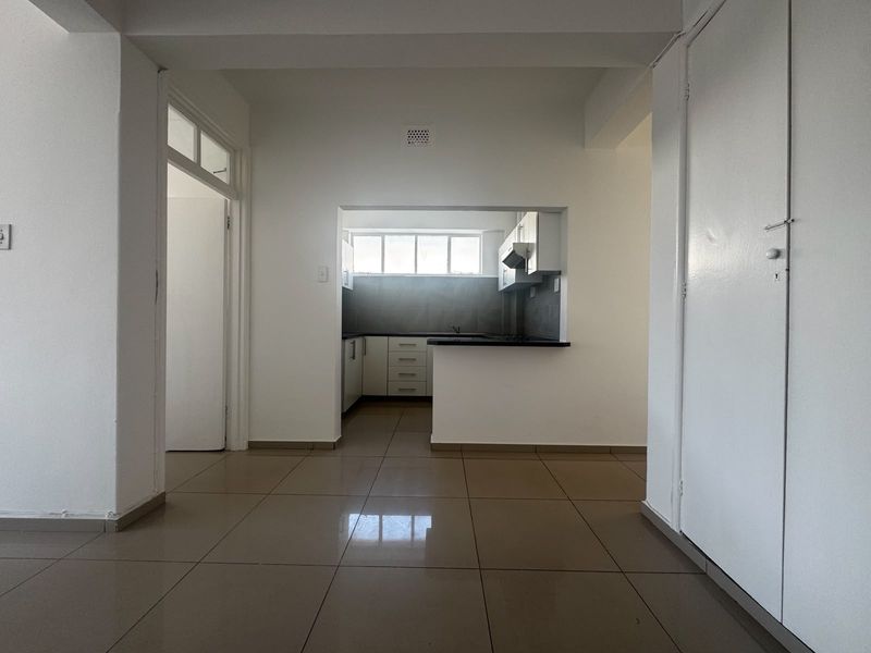 An open-plan living area featuring tiled flooring and a view into a functional kitchen with built-in cabinetry and an extractor fan.