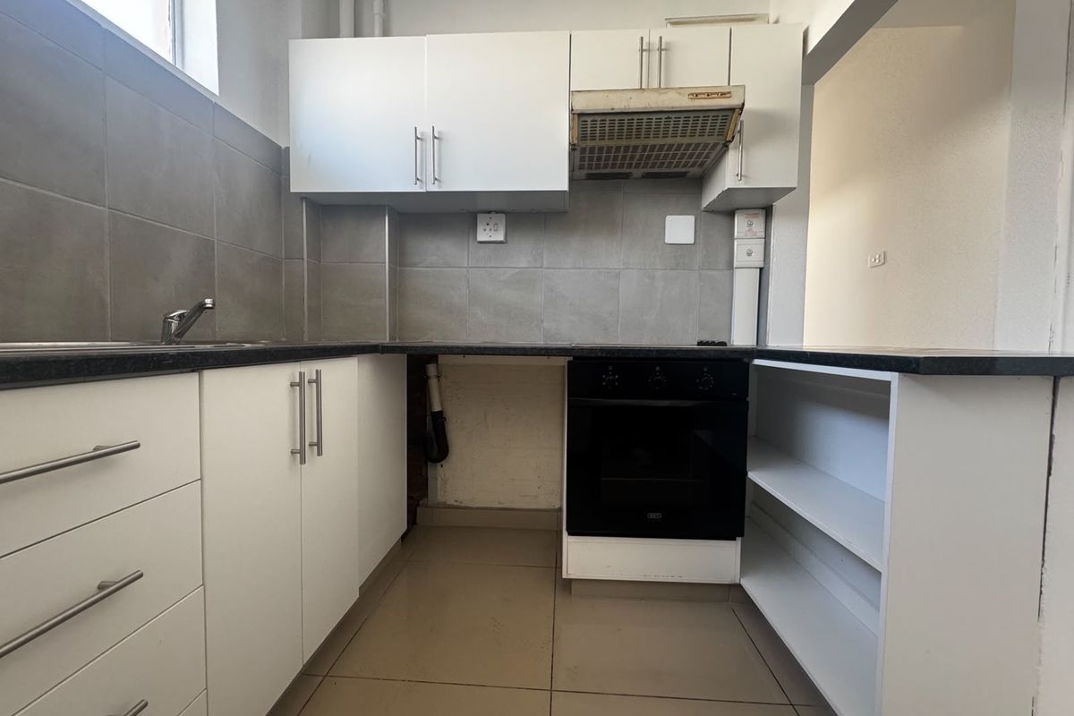 A compact kitchen featuring white cabinetry, a built-in oven, extractor fan, and tiled splashback, currently requiring minor repairs and cosmetic updates.