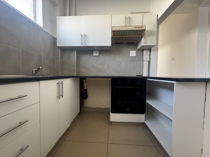 A compact kitchen featuring white cabinetry, a built-in oven, extractor fan, and tiled splashback, currently requiring minor repairs and cosmetic updates.