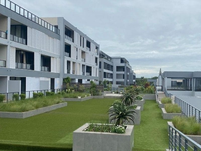A well-maintained communal rooftop garden area featuring artificial turf, raised concrete planters, and metal safety railings overlooking the apartment complex.