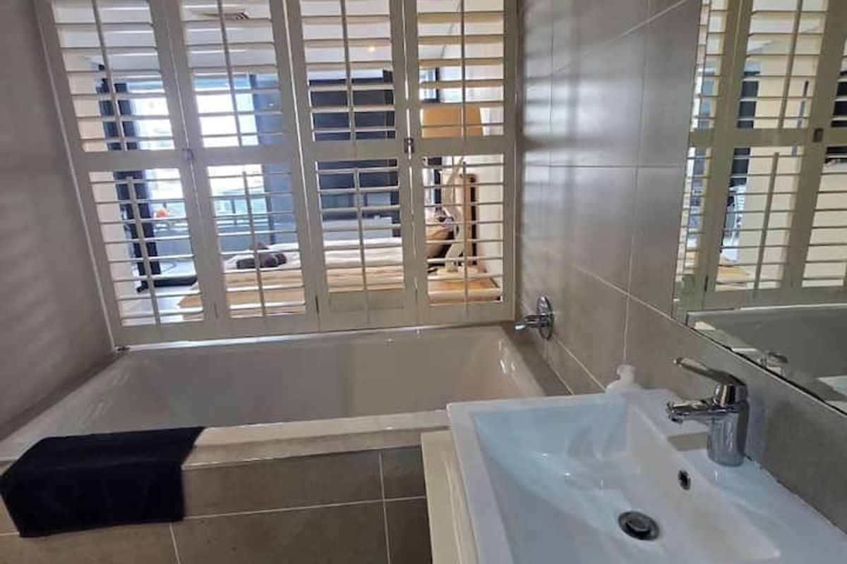 Modern bathroom featuring a built-in bathtub, vessel sink with chrome fixtures, and plantation shutters allowing natural light.