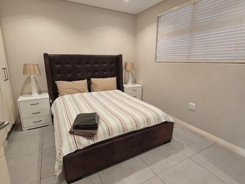 A well-maintained bedroom featuring neutral tiled flooring, recessed downlighting, ducted air conditioning, and venetian blinds for privacy.