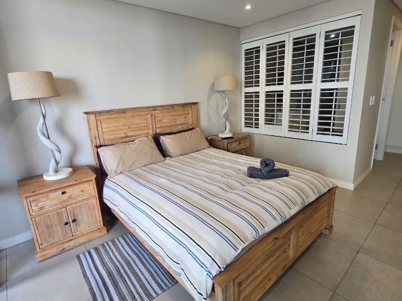 A well-maintained bedroom featuring neutral tiled flooring, plantation shutters, and integrated ceiling lighting with ducted air conditioning.