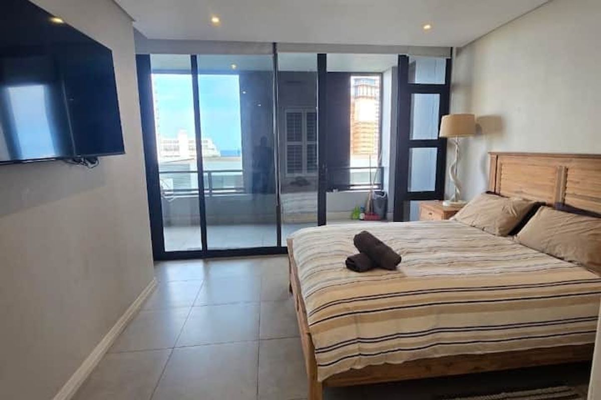 Spacious bedroom featuring large sliding glass doors leading to a balcony, neutral tiled flooring, and integrated ceiling lighting.