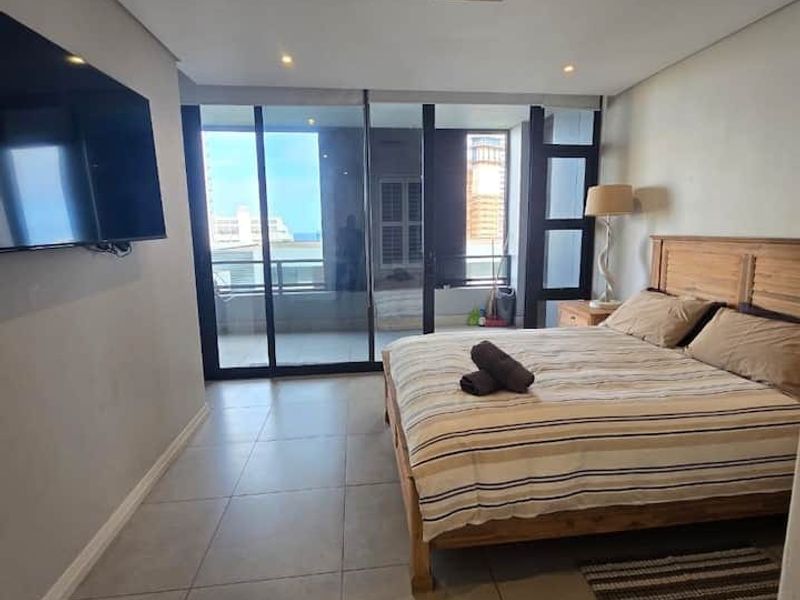 Spacious bedroom featuring large sliding glass doors leading to a balcony, neutral tiled flooring, and integrated ceiling lighting.