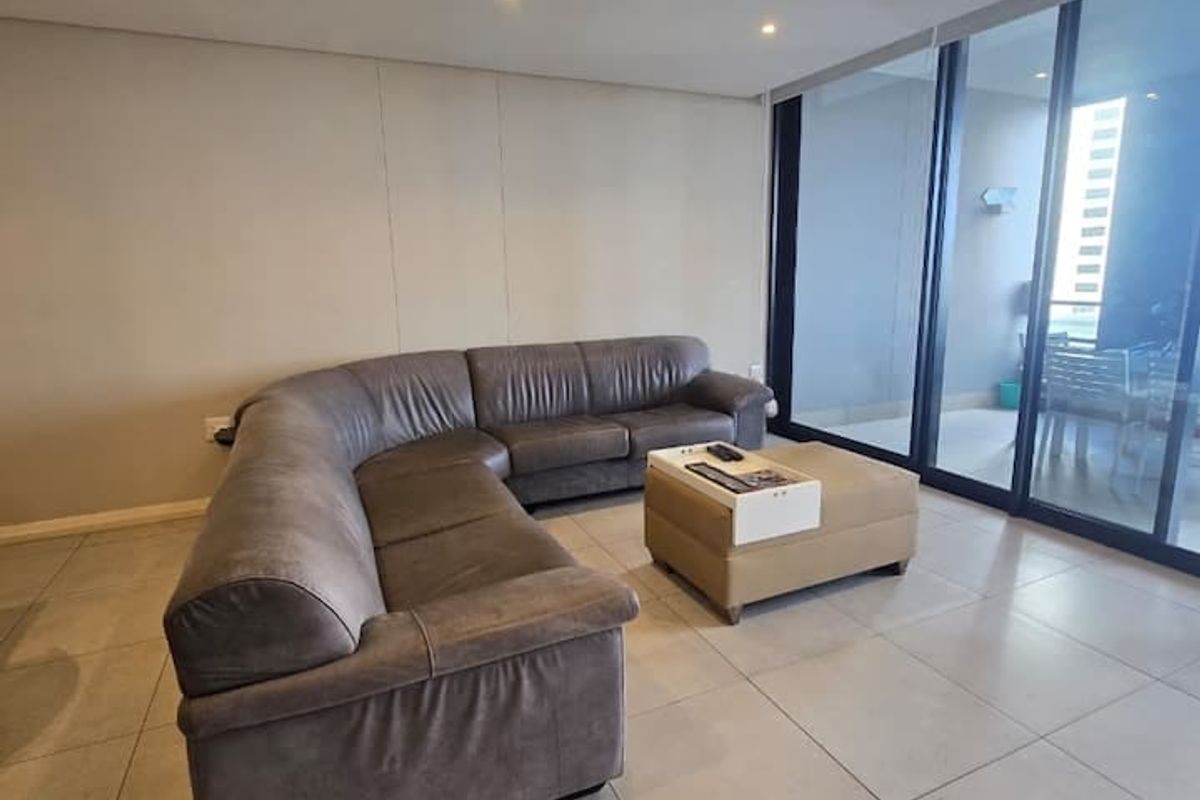 A modern living room featuring large format floor tiles, recessed downlighting, ducted air conditioning, and floor-to-ceiling sliding glass doors leading to a balcony.