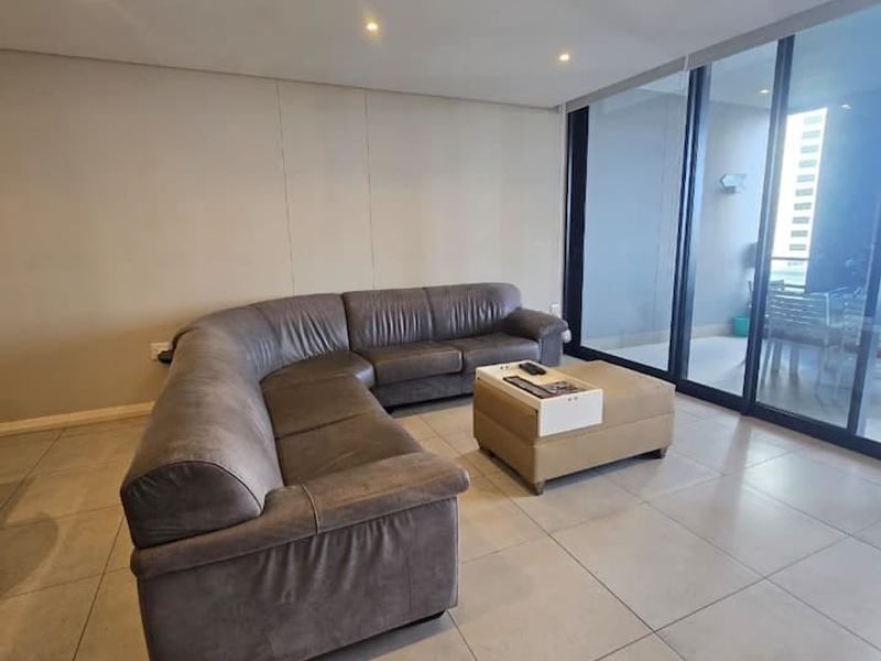 A modern living room featuring large format floor tiles, recessed downlighting, ducted air conditioning, and floor-to-ceiling sliding glass doors leading to a balcony.