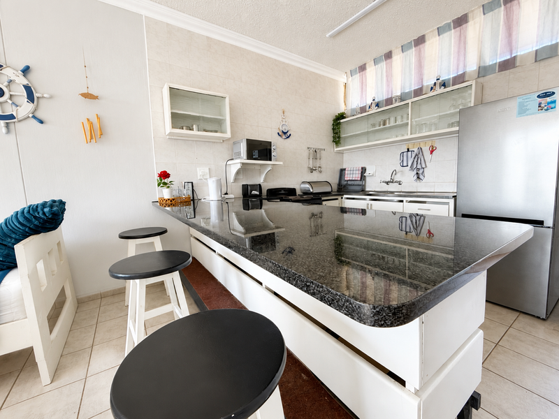 A functional kitchen featuring a large granite-topped breakfast bar, ample built-in cabinetry, tiled backsplash, and ceramic flooring.