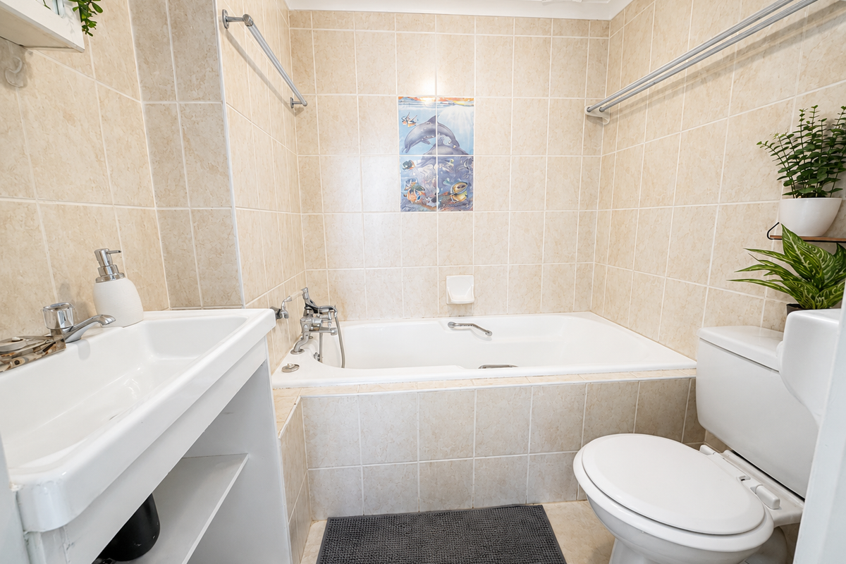A functional bathroom featuring a built-in bathtub, wall-mounted basin, and toilet, finished with neutral wall and floor tiling.