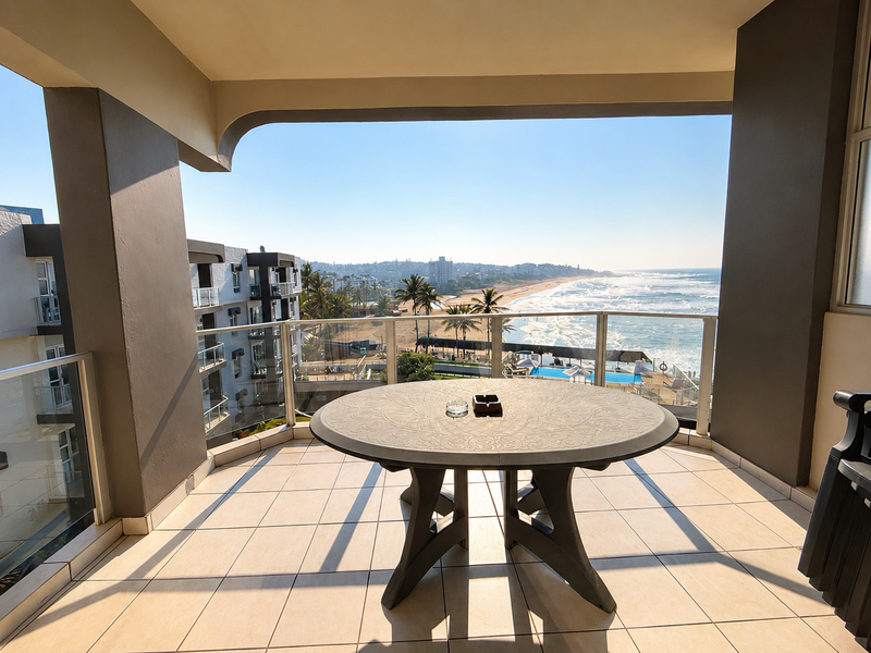A spacious covered balcony featuring tiled flooring and a glass balustrade, offering expansive ocean and coastal views.