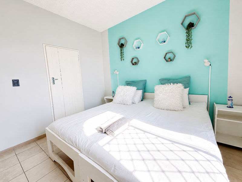 A bright bedroom featuring tiled flooring and a vibrant turquoise accent wall, providing a clean and functional sleeping space.