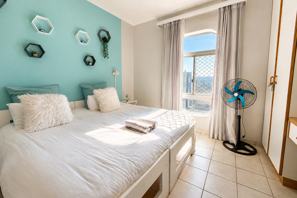 A bright bedroom featuring tiled flooring, a built-in wardrobe, and a window with security screening, offering natural light and a view.