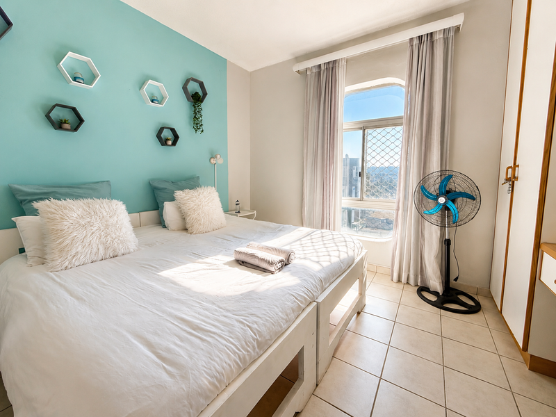 A bright bedroom featuring tiled flooring, a built-in wardrobe, and a window with security screening, offering natural light and a view.