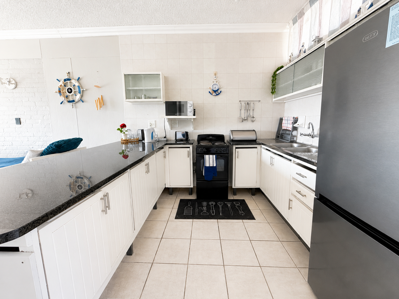 A functional kitchen featuring white cabinetry, granite countertops, a tiled backsplash, and a built-in electric stove with a double sink setup.