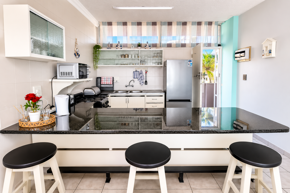 Functional kitchen featuring a granite breakfast bar, ample cabinetry, double basin sink, and tiled backsplash with direct access to an outdoor area.