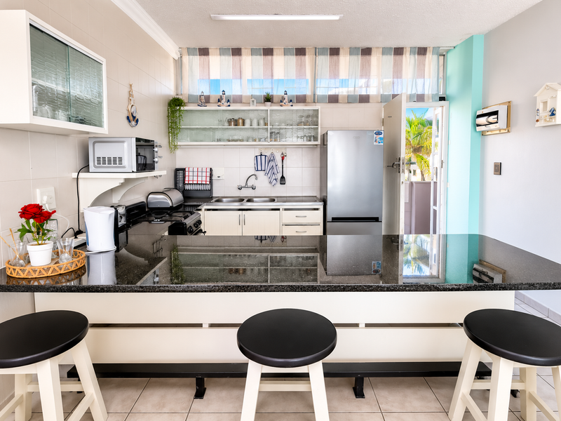 Functional kitchen featuring a granite breakfast bar, ample cabinetry, double basin sink, and tiled backsplash with direct access to an outdoor area.