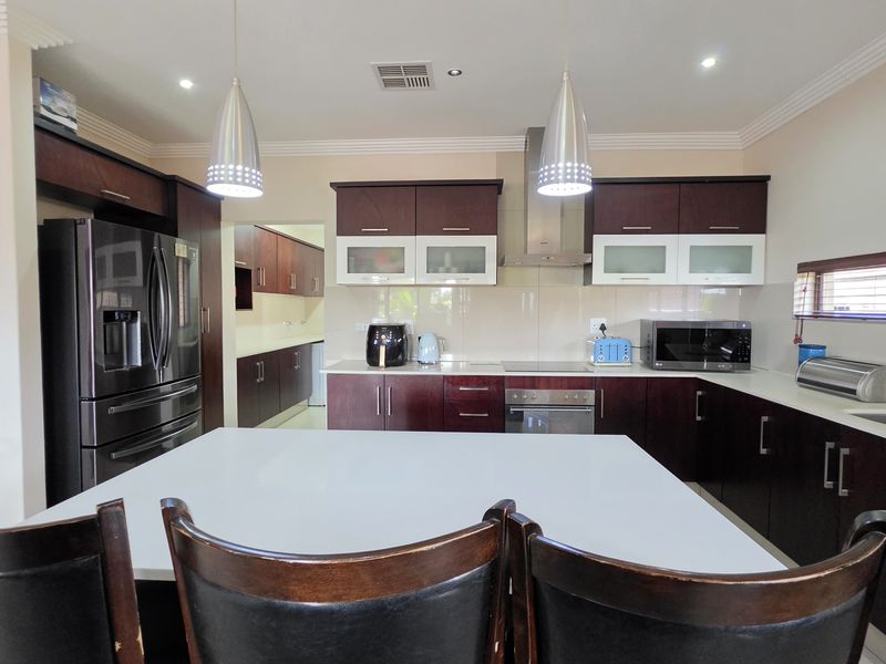 Modern kitchen featuring dark wood cabinetry, stone countertops, stainless steel appliances, and a central island, complemented by stylish pendant lighting.