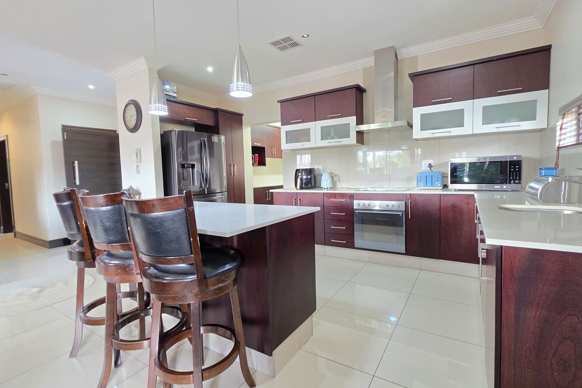 Modern kitchen featuring dark wood cabinetry, stone countertops, stainless steel appliances, and a central island with breakfast bar seating.