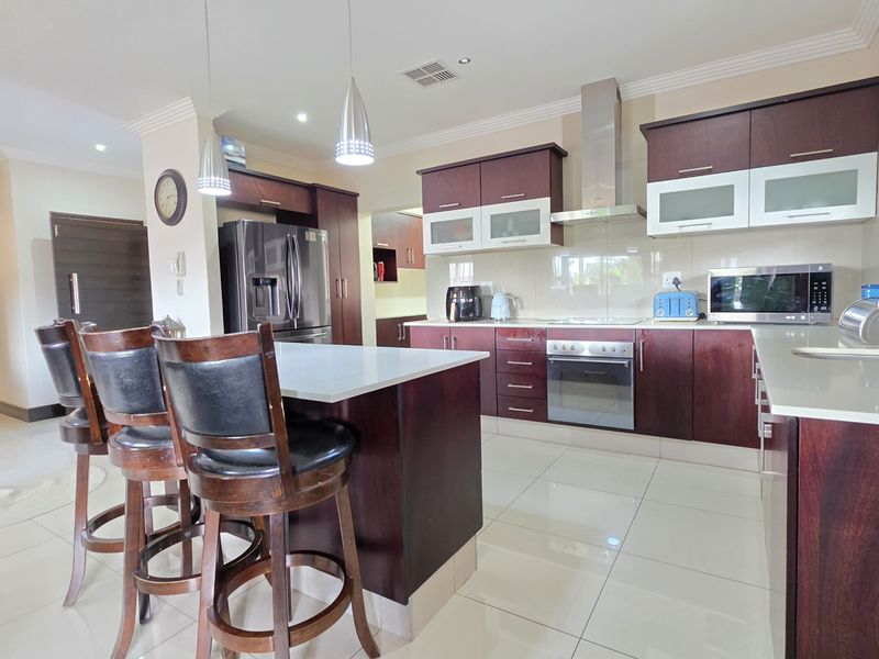 Modern kitchen featuring dark wood cabinetry, stone countertops, stainless steel appliances, and a central island with breakfast bar seating.